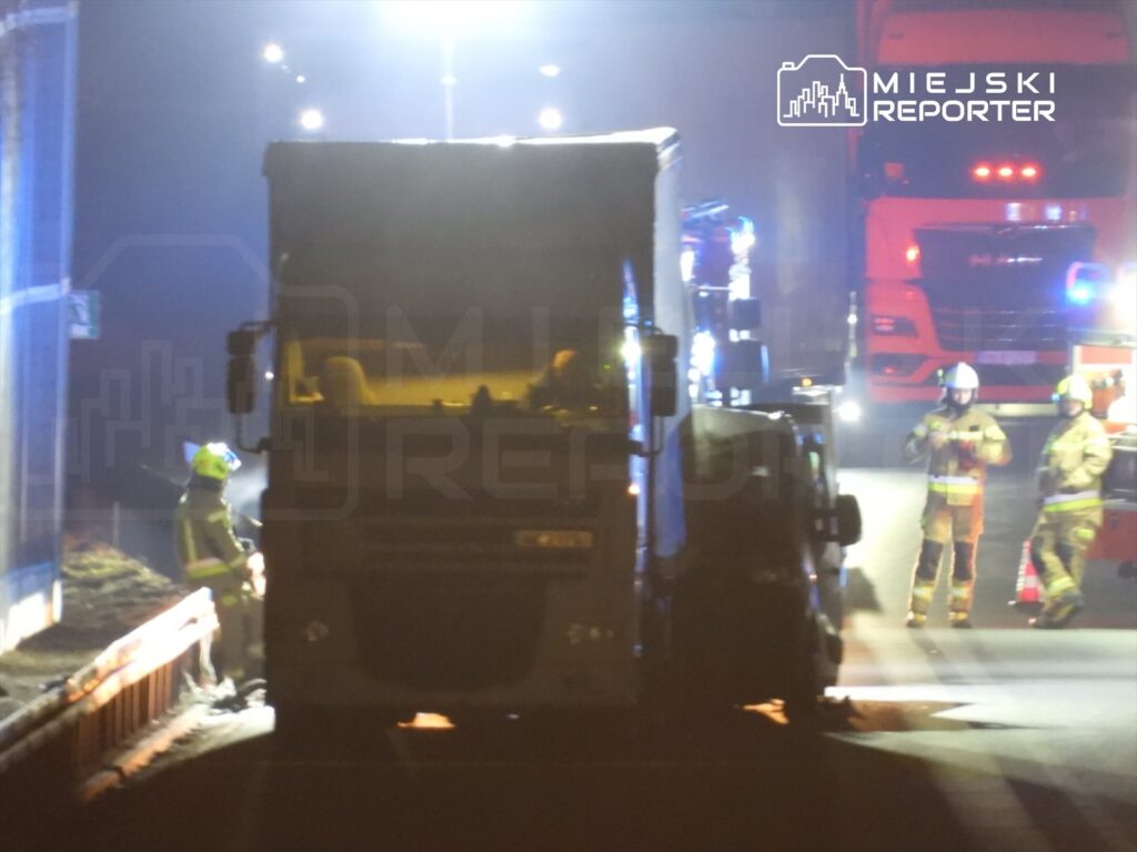 Strażacy w hełmach obserwują ciężarówkę na drodze, podczas nocnej akcji ratunkowej w oświetlonym miejscu.