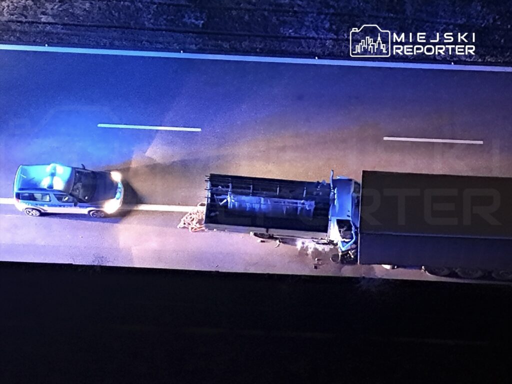 Policyjny radiowóz z niebieskimi światłami zatrzymany obok przewróconej ciężarówki na drodze.