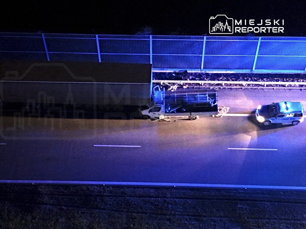 Policyjny radiowóz z niebieskimi sygnalizatorami zatrzymany obok ciężarówki na drodze w nocy.