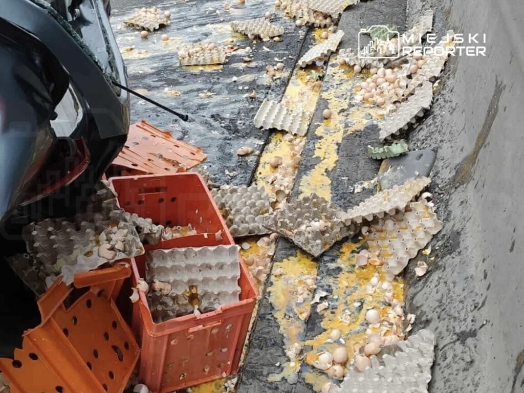 Na drodze leżą rozbite skorupki jajek oraz porzucone kartony po jajkach. W tle widać fragment pojazdu.