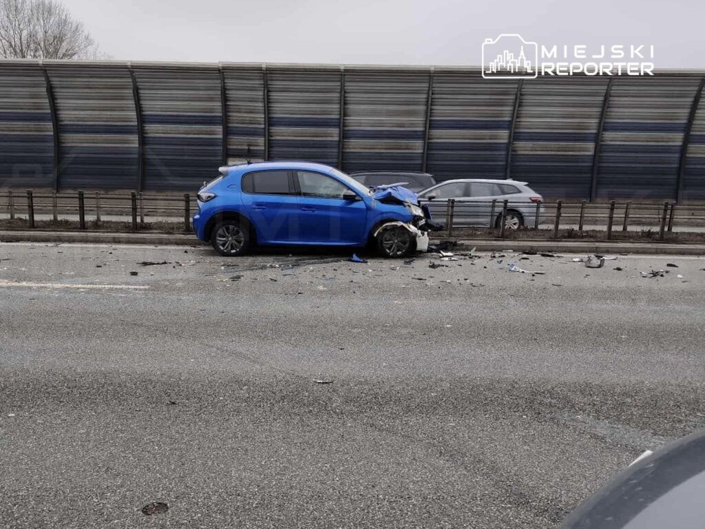 Niebieski samochód osobowy z uszkodzoną przednią częścią stoi na poboczu drogi, otoczony odłamkami szkła.