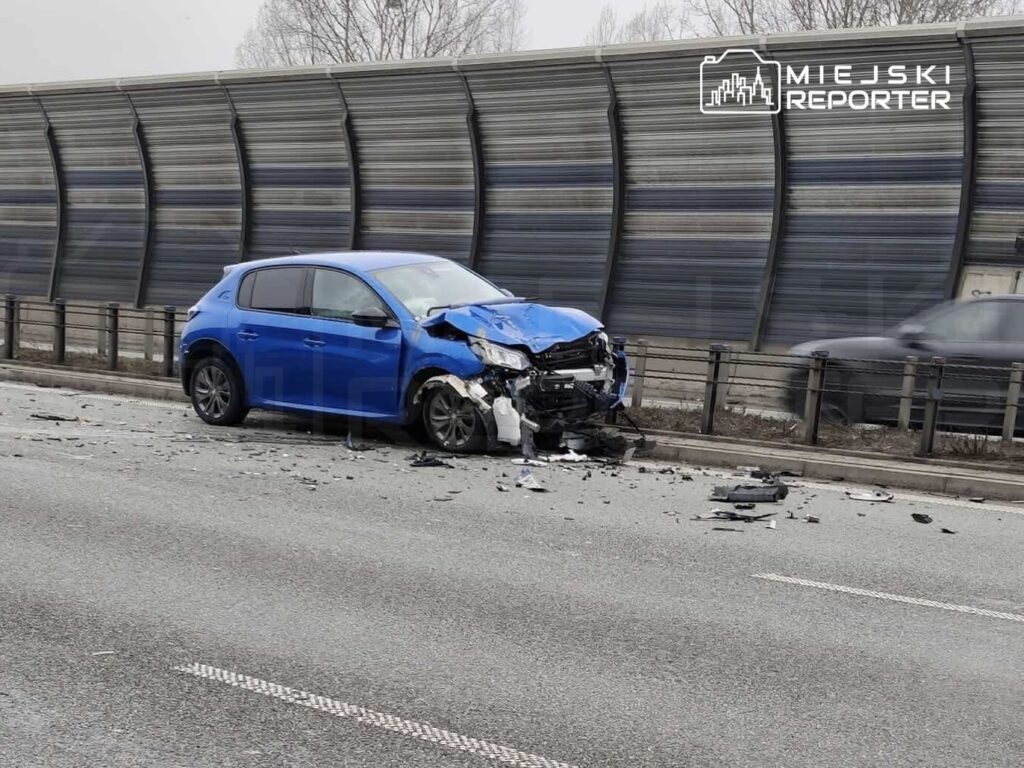 Zniszczony niebieski samochód osobowy stoi na drodze, otoczony odłamkami po wypadku.