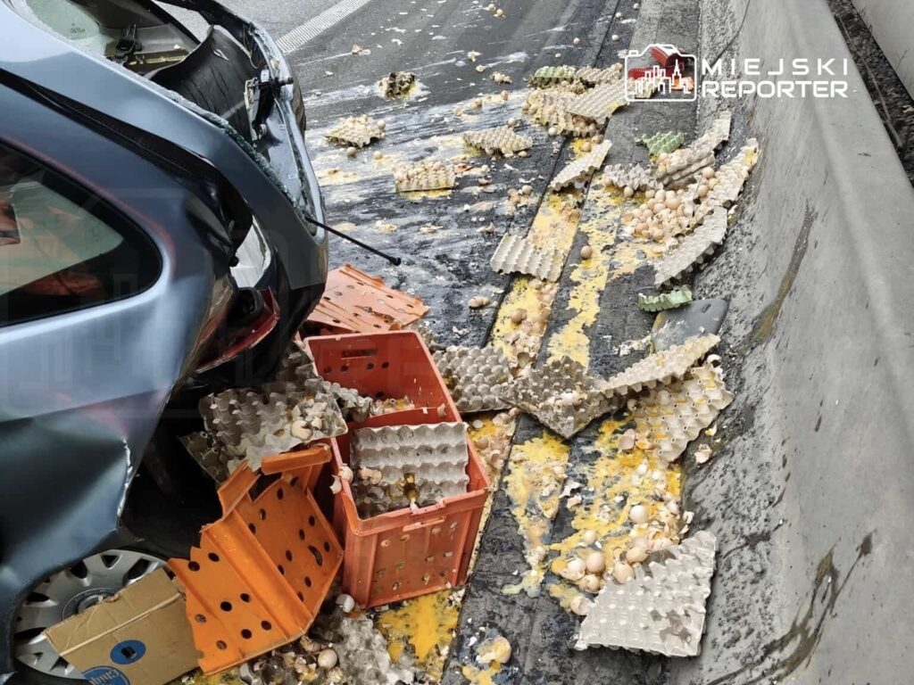Zniszczony samochód z otwartą klapą, z której wylatują kartony z jajkami na jezdnię.