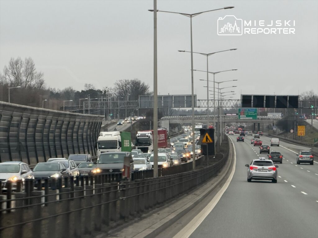 Korki na drodze ekspresowej, z pojazdami poruszającymi się w obu kierunkach, w szarym, pochmurnym otoczeniu.