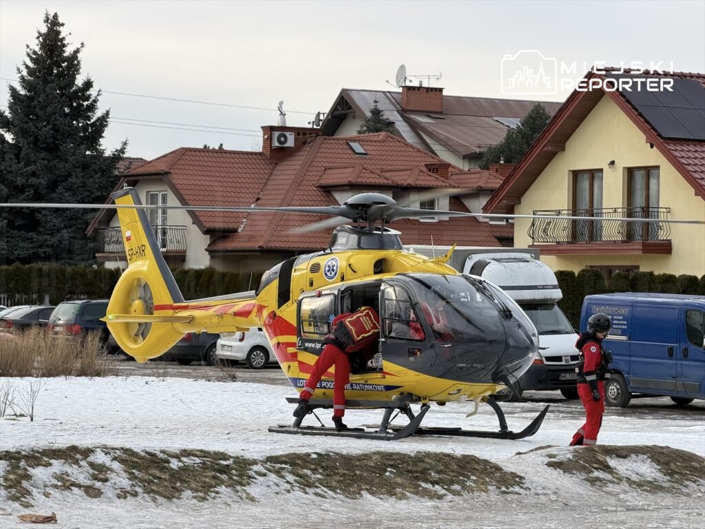 Lądowanie śmigłowca ratunkowego na śnieżnym terenie, obok dwóch ratowników przygotowujących się do akcji.