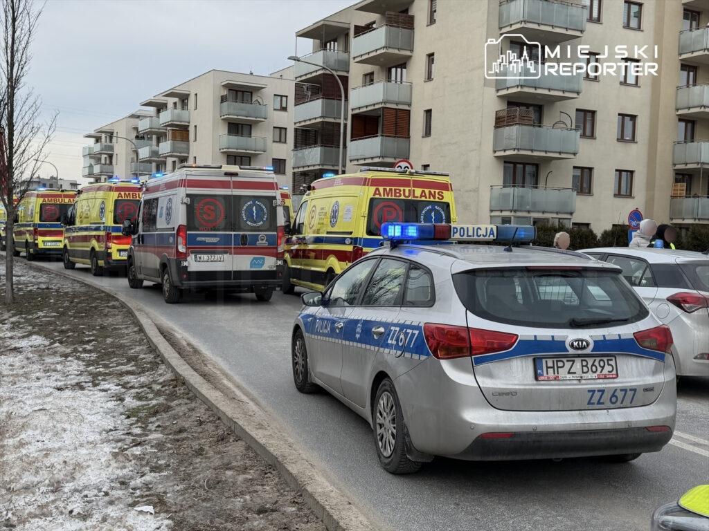 Karetki pogotowia oraz radiowóz policji zatrzymane wzdłuż ulicy w pobliżu budynków mieszkalnych.
