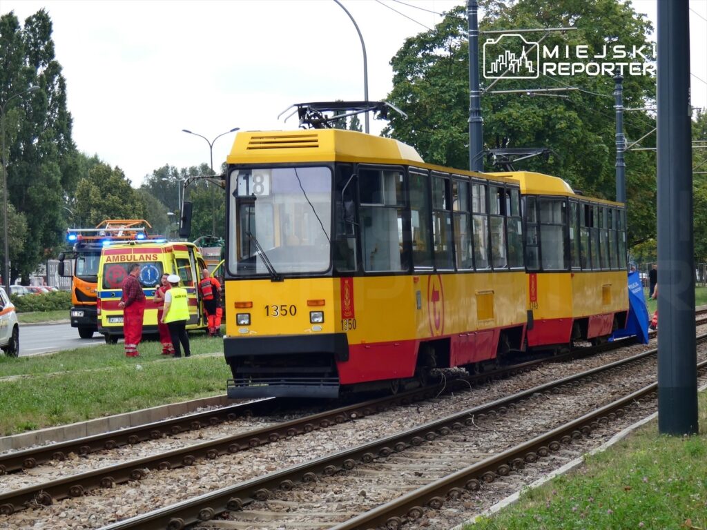 Żółty tramwaj stoi na torach, obok grupy ratowników medycznych i ambulansu z włączonymi sygnałami świetlnymi.