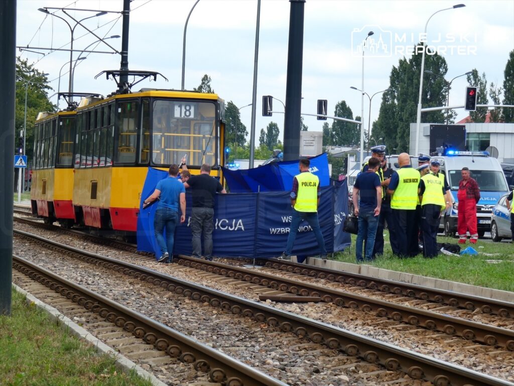 Policjanci oraz ratownicy medyczni zabezpieczają miejsce zdarzenia przy torowisku tramwajowym.