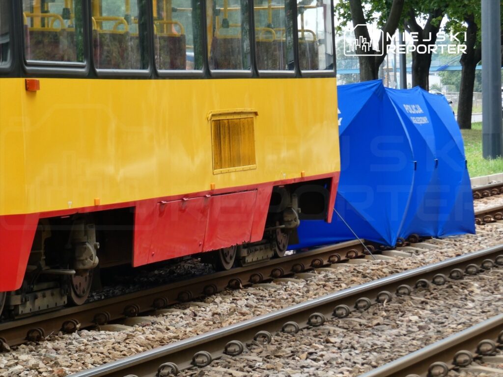 Żółty tramwaj stoi na torach, obok znajduje się niebieski namiot policyjny.
