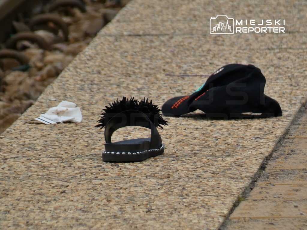 Czarna klapka z ozdobnym futerkiem leży na peronie obok ciemnej czapki i kawałka papieru.