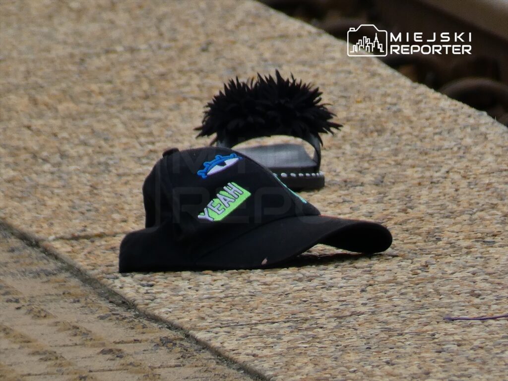 Czarna czapka z napisem "YEAH" leży na chodniku obok klapek z ozdobnym pomponem.