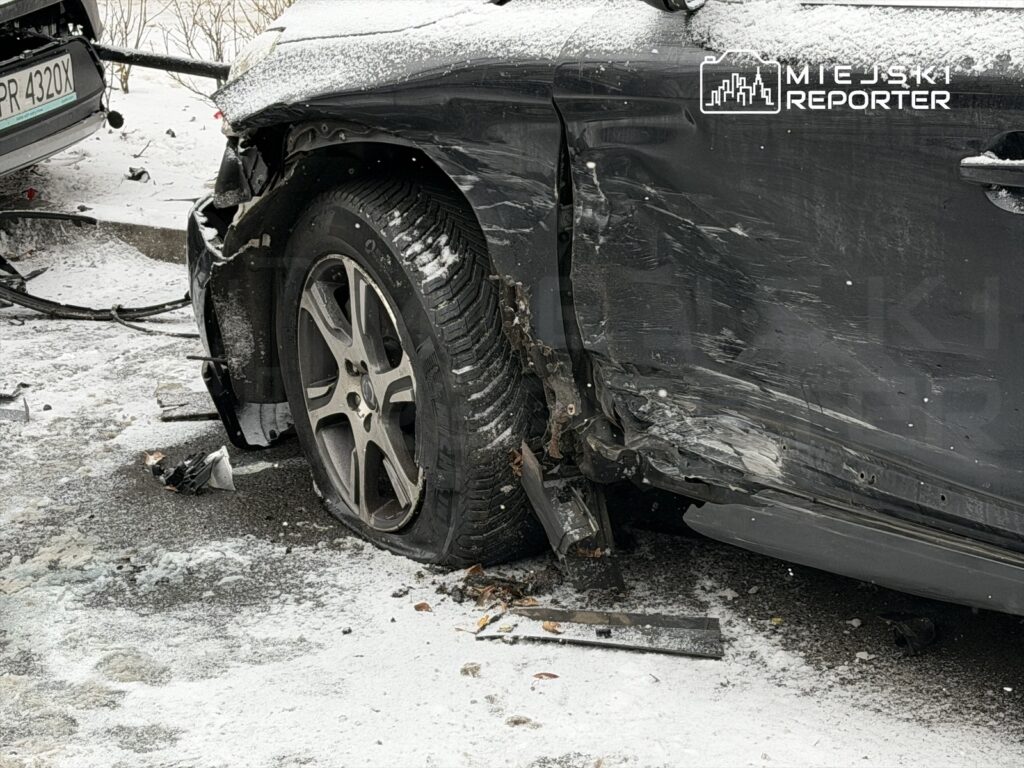 Uszkodzony samochód osobowy z odgiętą karoserią i przebitą oponą na zaśnieżonej nawierzchni.