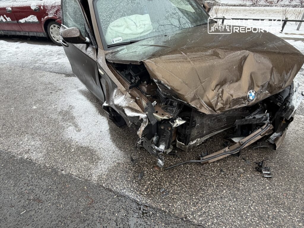 Uszkodzony samochód osobowy marki BMW z rozdartą maską i uszkodzonym przodem, zaparkowany na ośnieżonej ulicy.