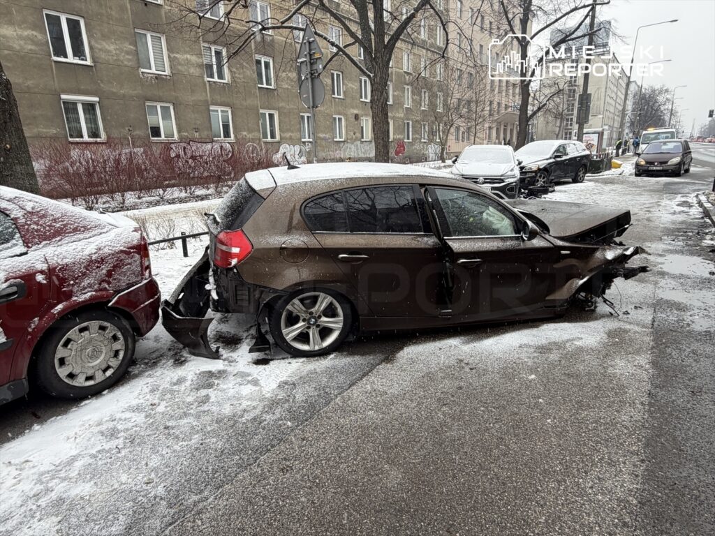 Dwa uszkodzone samochody zaparkowane na śnieżnej ulicy, w tle widoczny budynek mieszkalny.