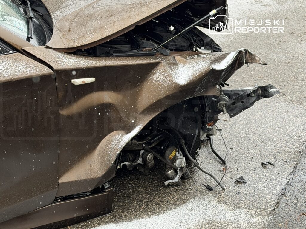 Uszkodzona karoseria brązowego samochodu osobowego z wgnieceniem na przednim błotniku i odsłoniętymi elementami mechanicznymi.