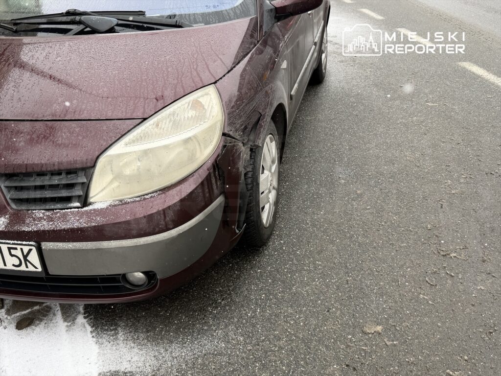 Czerwony samochód osobowy z uszkodzoną przednią częścią zaparkowany na mokrej drodze.