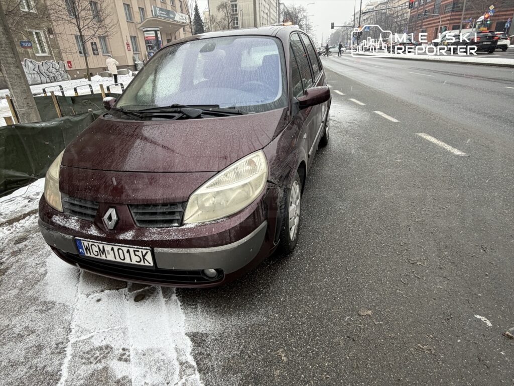 Czerwony samochód osobowy zaparkowany na zaśnieżonej ulicy w miejskim otoczeniu.