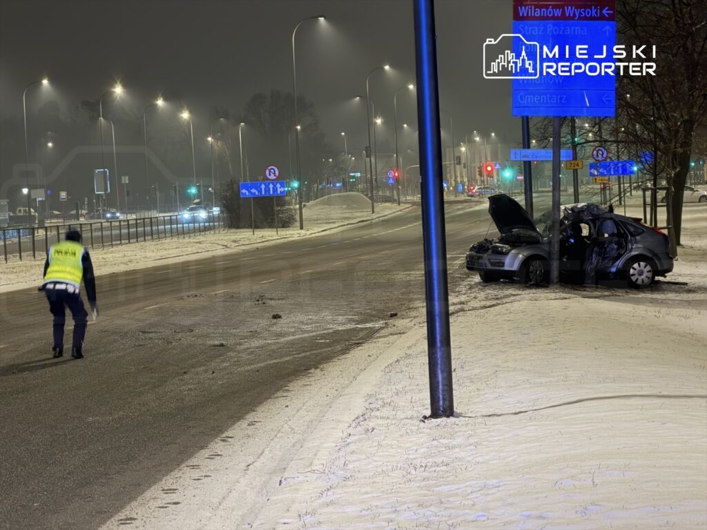 Policjant w odblaskowej kamizelce zbiera dowody na ośnieżonej jezdni obok uszkodzonego samochodu.