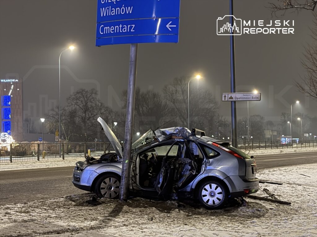 Zniszczony samochód osobowy uderzył w słup, zaparkowany na zaśnieżonej ulicy, obok znaków drogowych.