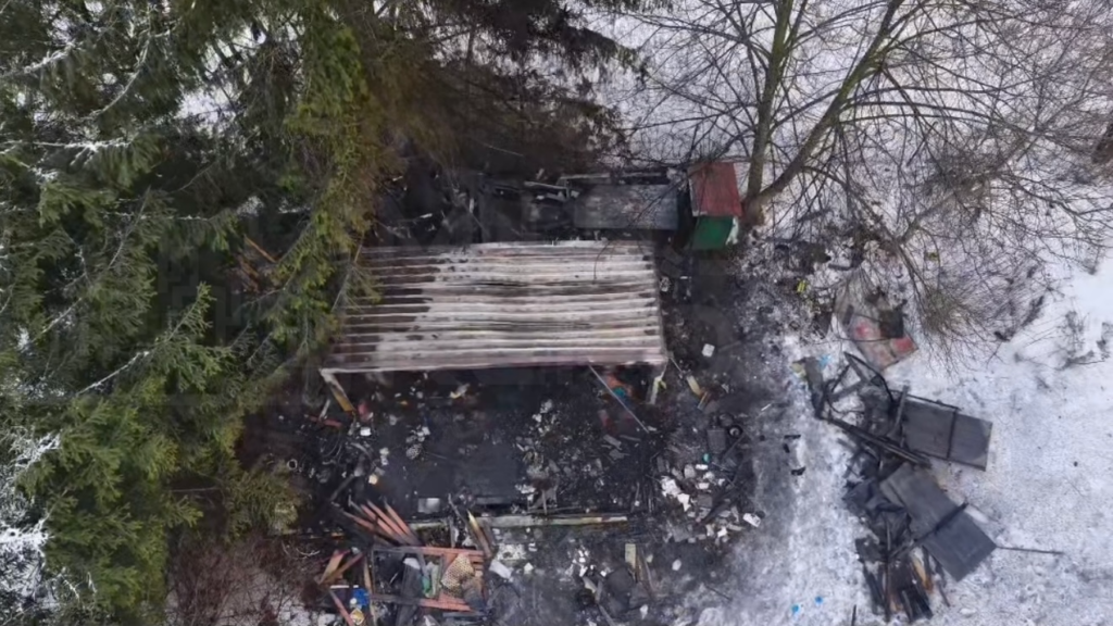 Zniszczona konstrukcja w otoczeniu zarośli, z widocznymi śladami po pożarze i porozrzucanymi odpadami.