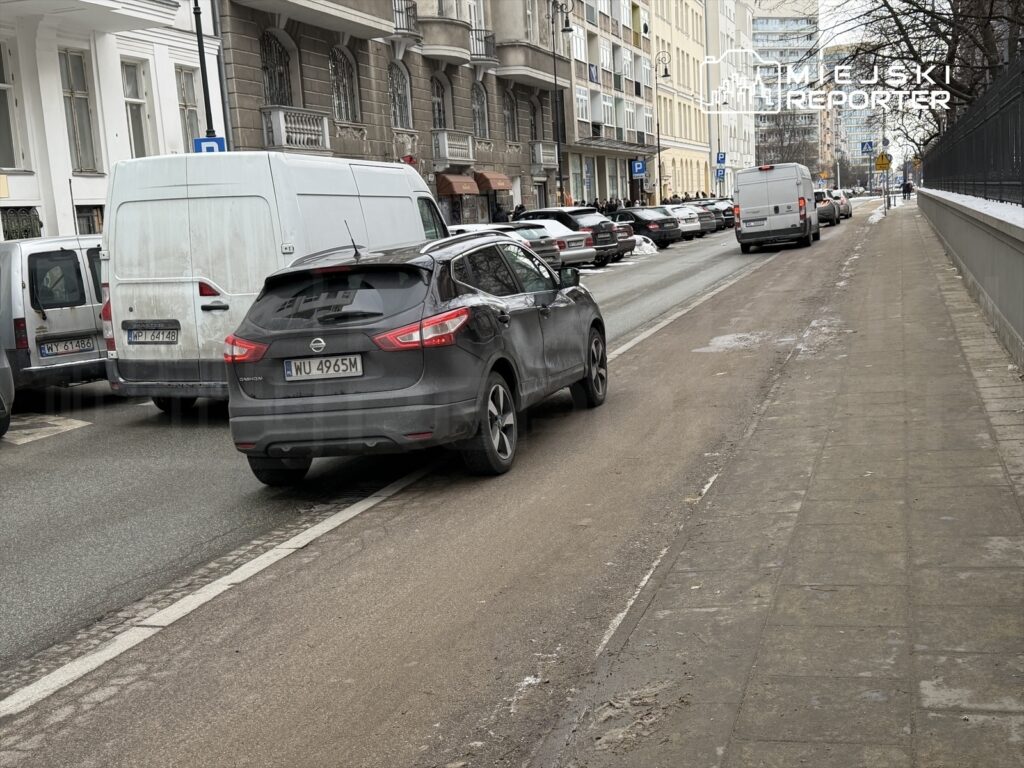 Czarny samochód osobowy zaparkowany obok białego furgonu na miejskiej ulicy w zimowej scenerii.