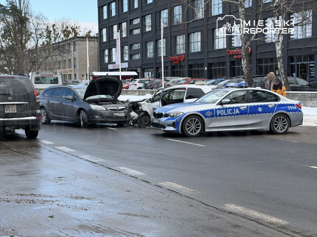Dwa uszkodzone samochody osobowe oraz radiowóz policyjny na ruchliwej ulicy w mieście.