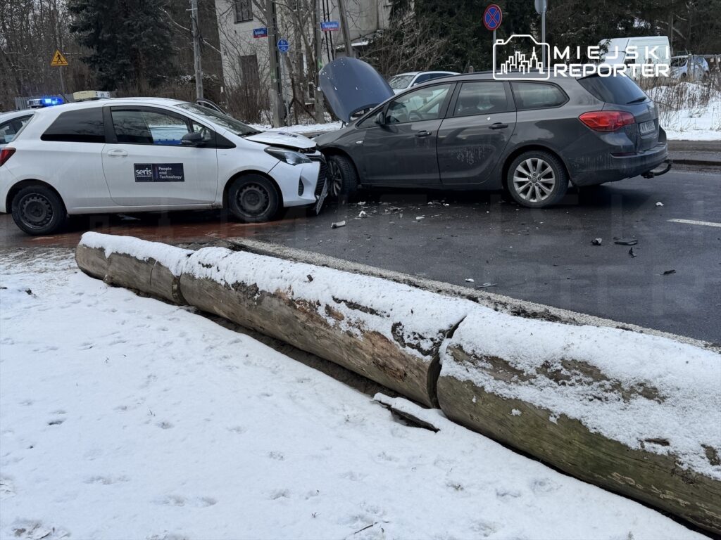 Zderzenie dwóch samochodów osobowych na zaśnieżonej ulicy, z widoczną uszkodzoną przednią częścią pojazdu.