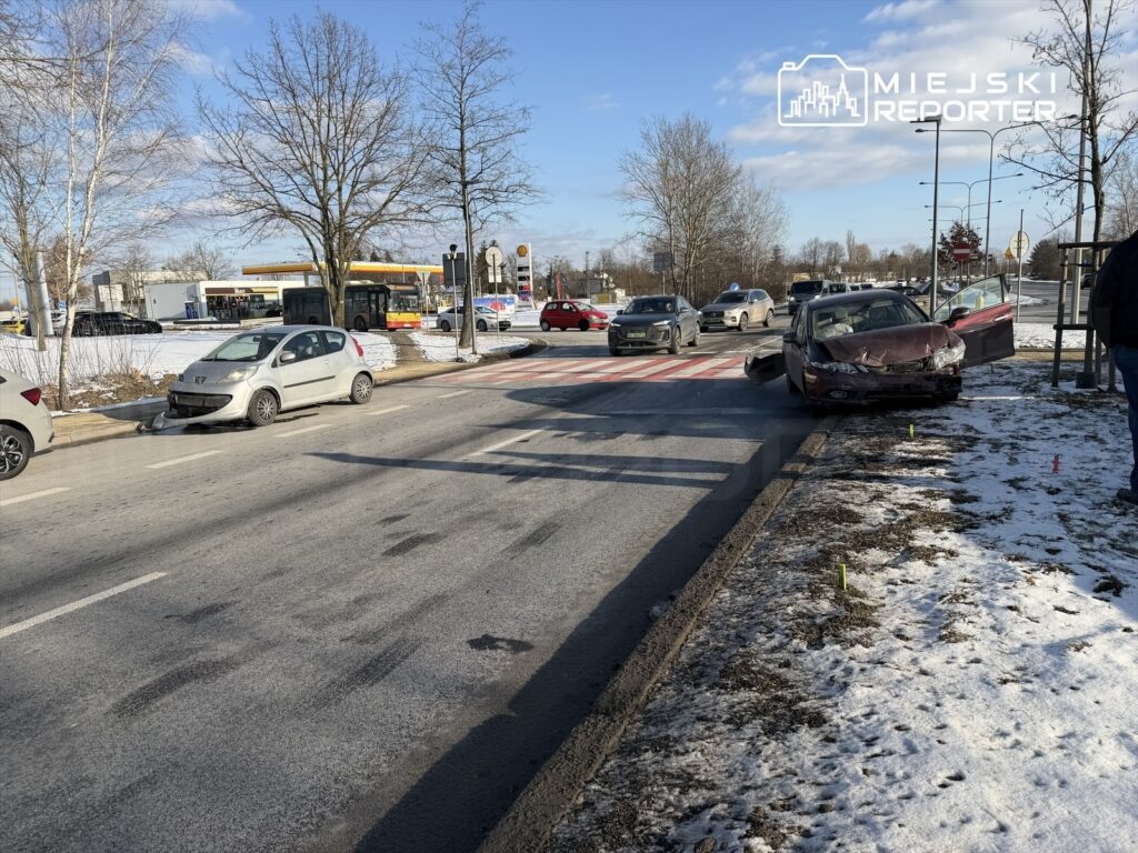 W zderzeniu drogowym uczestniczą dwa uszkodzone samochody, jeden stoi na poboczu, a drugi na jezdni w zimowej scenerii.