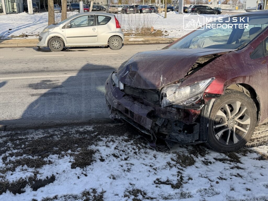 Czerwony samochód osobowy z uszkodzoną przednią częścią stoi na poboczu oblodzonej drogi, obok srebrnego auta.