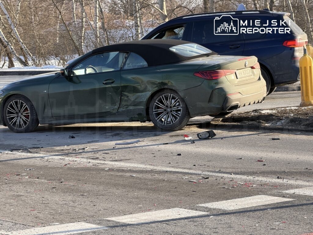 Zielony kabriolet z uszkodzoną boczną częścią stoi na jezdni obok drugiego pojazdu, wokół leżą resztki zderzenia.