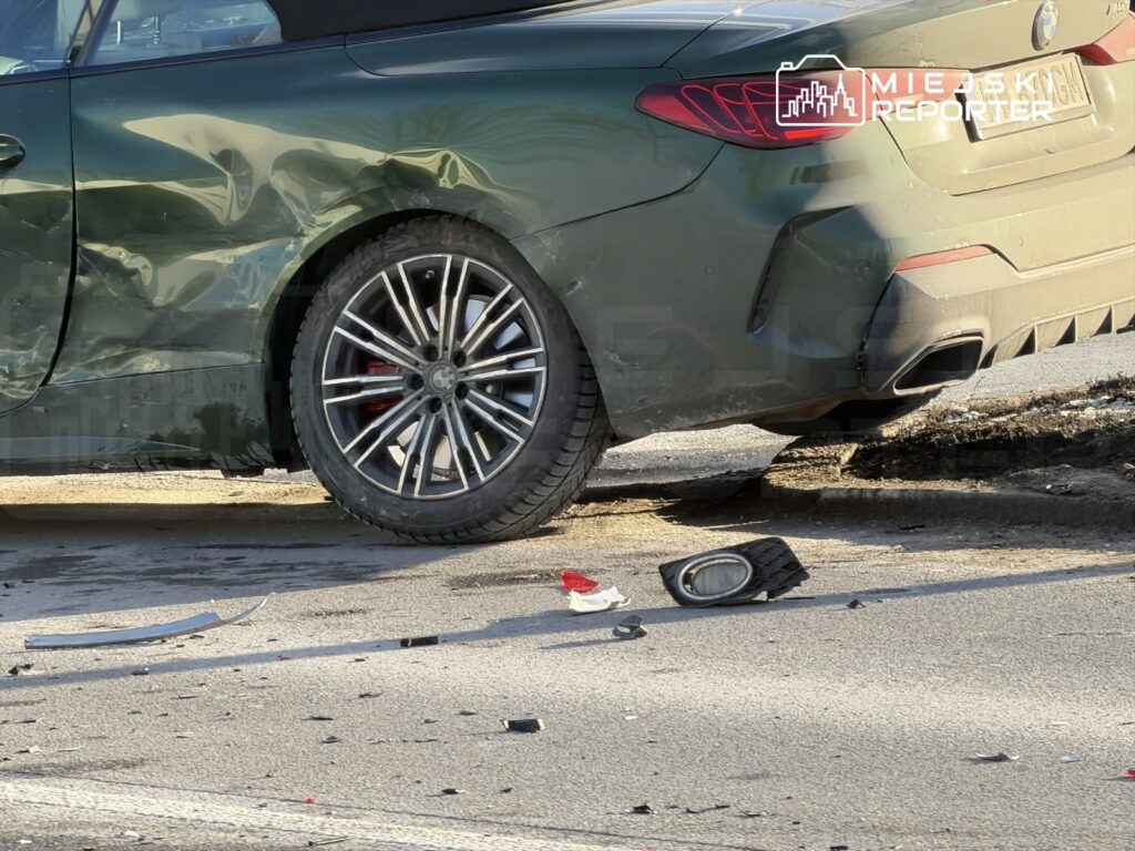 Zniszczony samochód osobowy na poboczu drogi, obok porozrzucane fragmenty karoserii i uszkodzone elementy pojazdu.