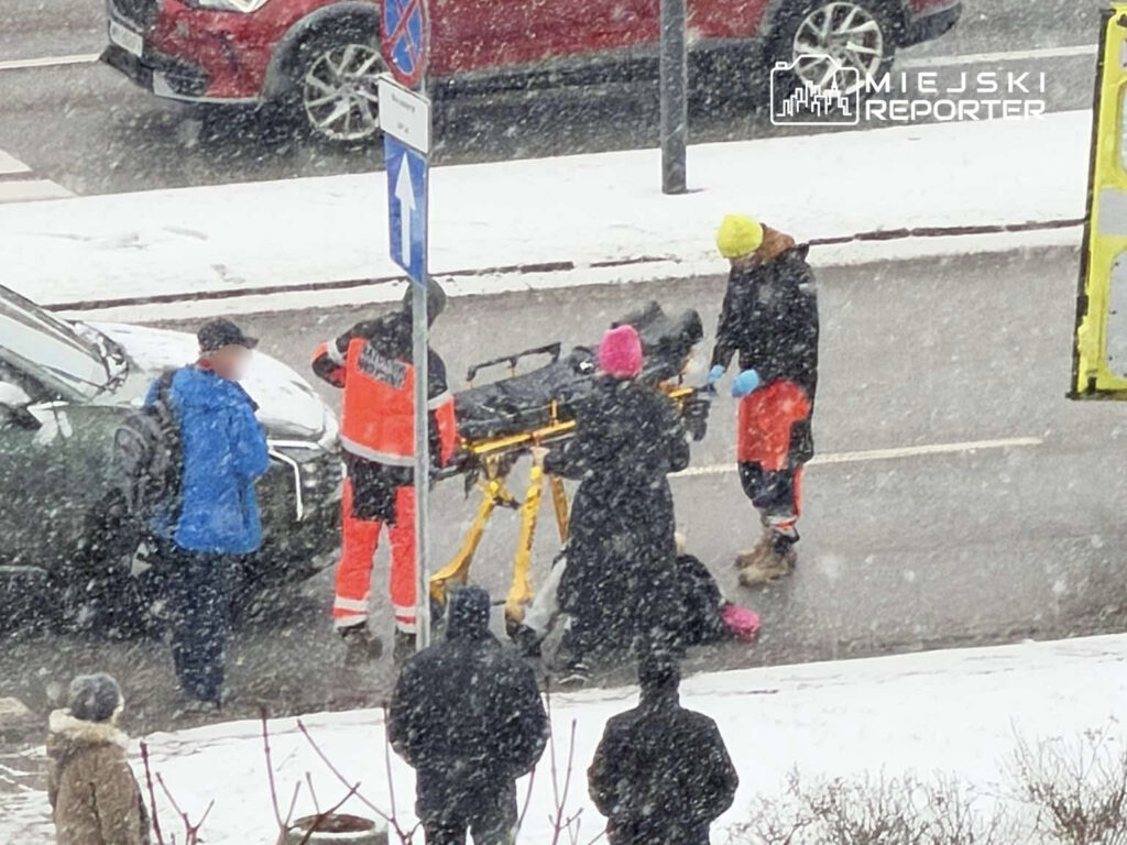 Grupa ratowników medycznych udziela pomocy osobie leżącej na noszach w zaśnieżonym otoczeniu.