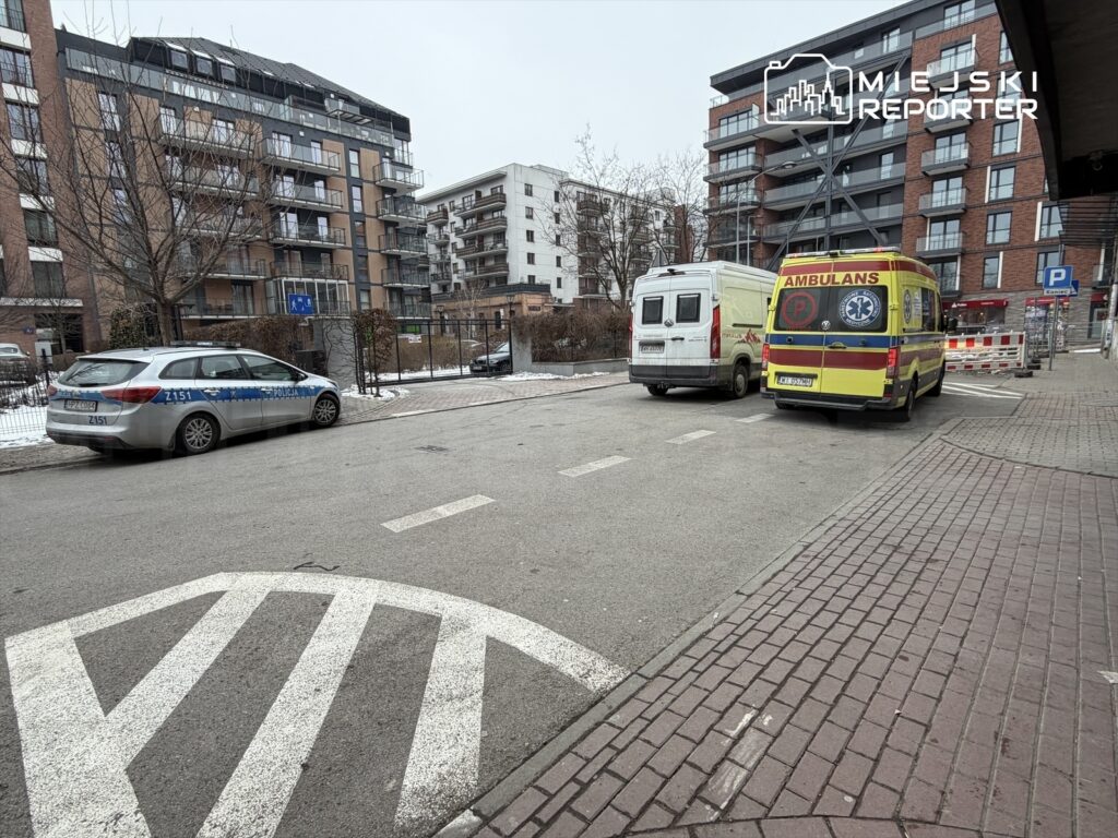 Policyjny radiowóz oraz ambulans zaparkowane na ulicy w miejskim otoczeniu, obok nowoczesnych budynków mieszkalnych.