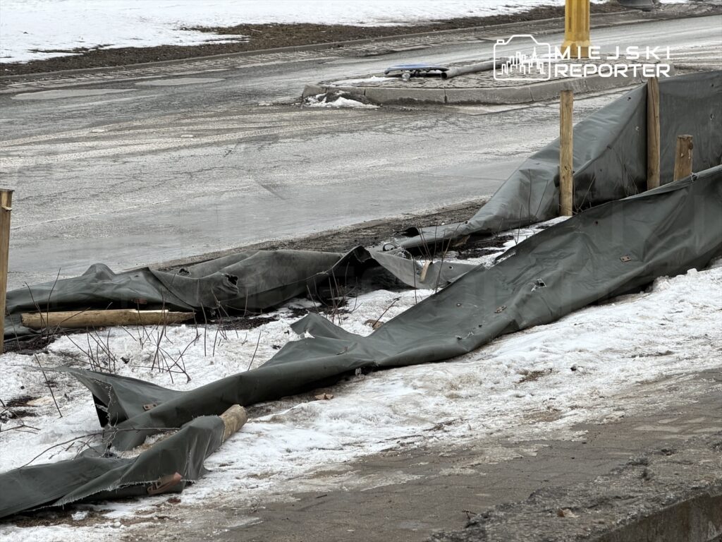 Na ziemi leżą rozciągnięte, uszkodzone plandeki w otoczeniu śniegu i mokrej nawierzchni drogi.