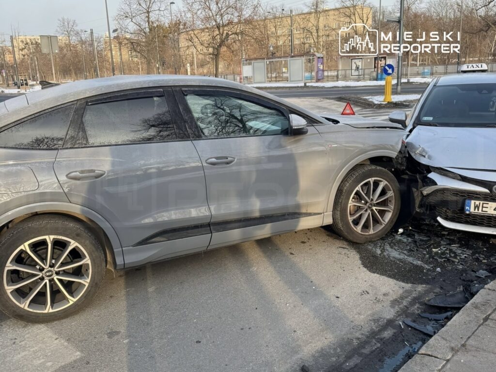 Dwa uszkodzone samochody osobowe stoją na ulicy po kolizji; szary pojazd uderzył w taksówkę.