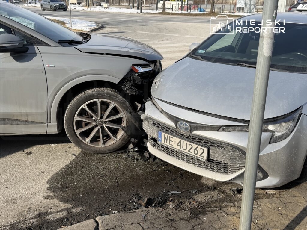 Dwa uszkodzone samochody osobowe stoją obok siebie na ulicy, jeden z nich z wgniecioną maską.