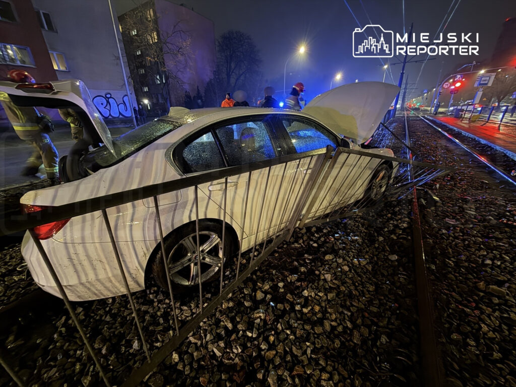 Biały samochód osobowy stoi na torach tramwajowych, obok grupy strażaków i osób w odblaskowych kamizelkach.