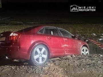 Czerwony samochód osobowy utknął w błocie na nieutwardzonej drodze w nocy.