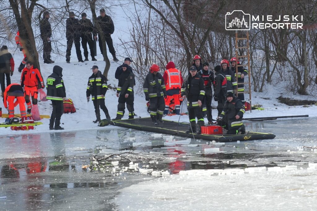 Grupa ratowników w odzieży ochronnej przygotowuje sprzęt na zamarzniętej rzece w zimowym otoczeniu.