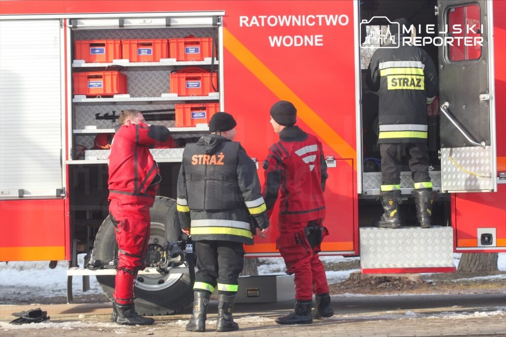 Czterech ratowników w specjalistycznym ubraniu rozmawia przy pojeździe ratownictwa wodnego, przygotowując sprzęt.