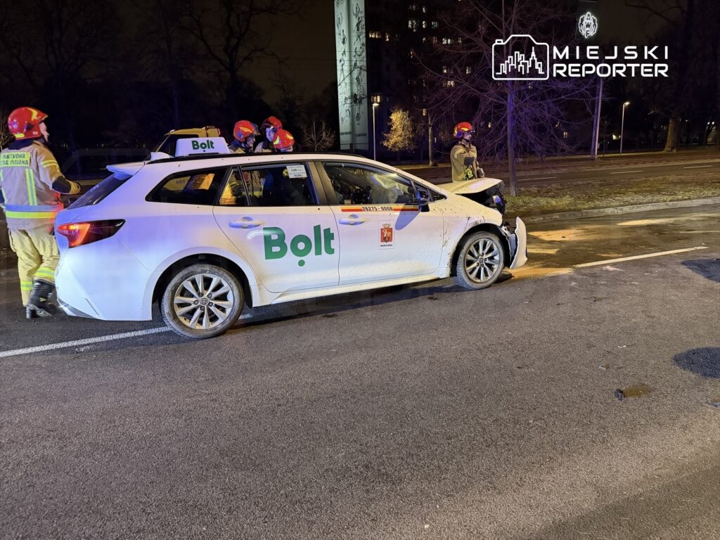 Zespół ratunkowy pracuje przy uszkodzonym samochodzie Bolt na oświetlonej ulicy.