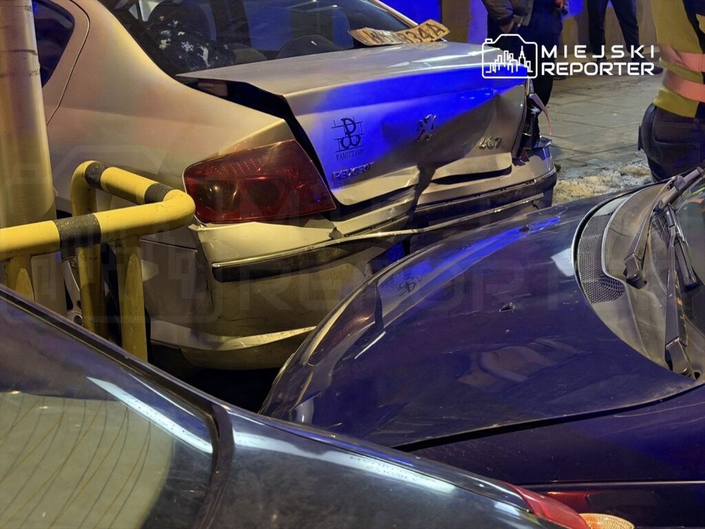 Zderzone samochody na ulicy, z widocznymi uszkodzeniami tylnych części pojazdów oraz policyjnym oświetleniem w tle.