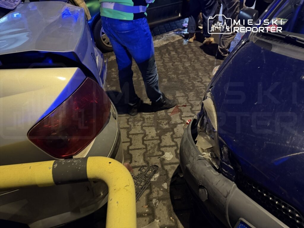 Mężczyzna w odblaskowej kamizelce bada uszkodzone samochody na parkingu po kolizji.