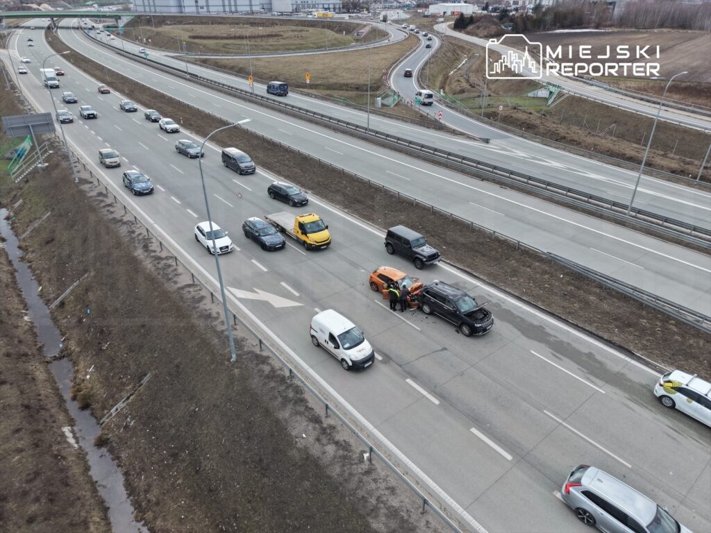 Kolizja drogowa z udziałem dwóch samochodów osobowych na jezdni, obok ruchu samochodowego w tle.