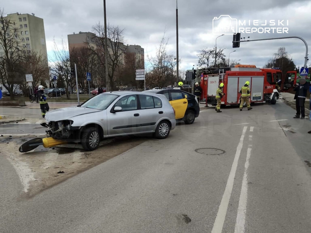 Dwa uszkodzone samochody na skrzyżowaniu, obok działa ekipa strażacka w akcji ratunkowej.
