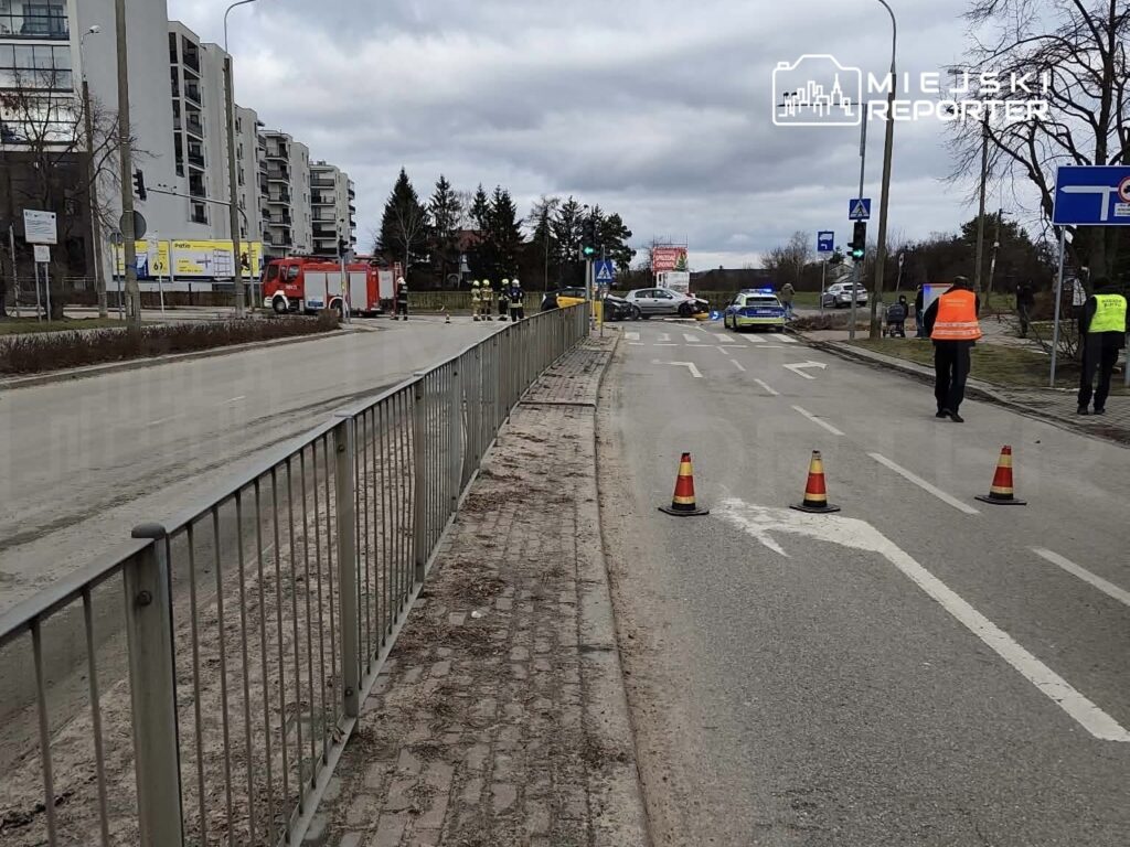 Na skrzyżowaniu ulicy stoją pojazdy straży pożarnej i policji, a funkcjonariusze kierują ruchem.