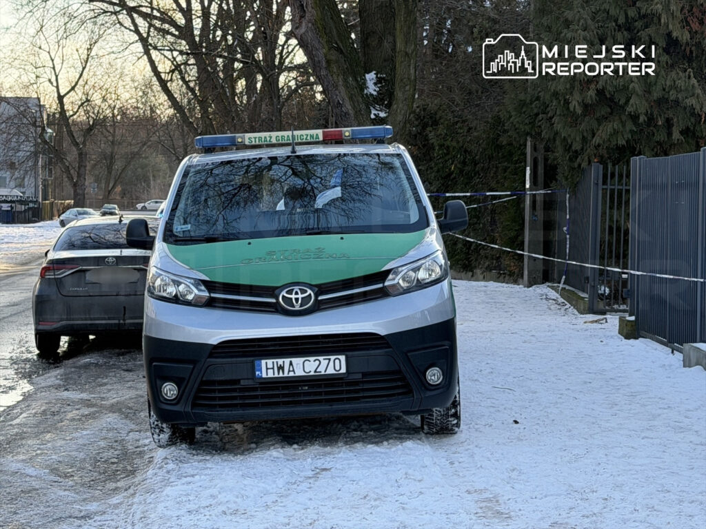 Samochód Straży Granicznej z włączonymi sygnałami świetlnymi zaparkowany na zaśnieżonej ulicy.