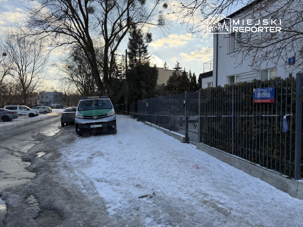 Zielony samochód służbowy zaparkowany na ośnieżonej ulicy, obok ogrodzenia z tabliczką "Edisona".