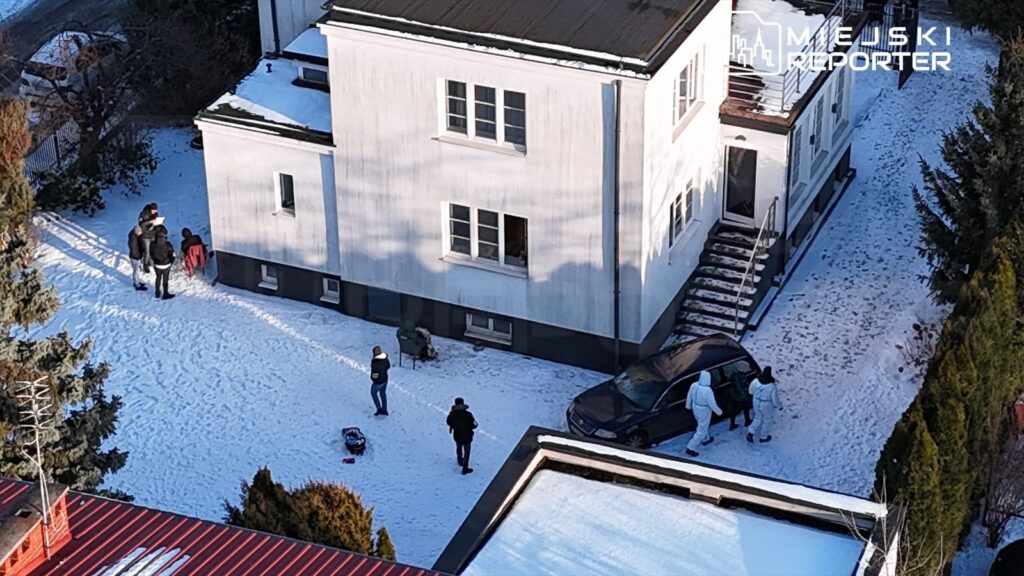 Grupa osób w zimowych ubraniach bawi się na zaśnieżonym terenie obok nowoczesnego budynku.