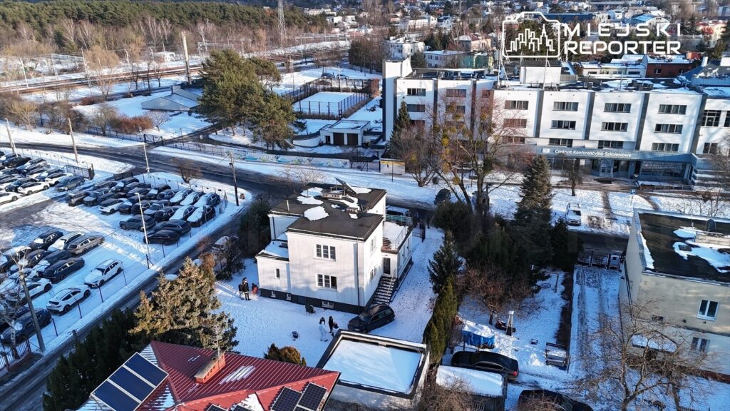 Widok z lotu ptaka na osiedle z nowoczesnym domem, parkingiem i śnieżnym otoczeniem, w tle Centrum Konferencyjno-Szkoleniowe.